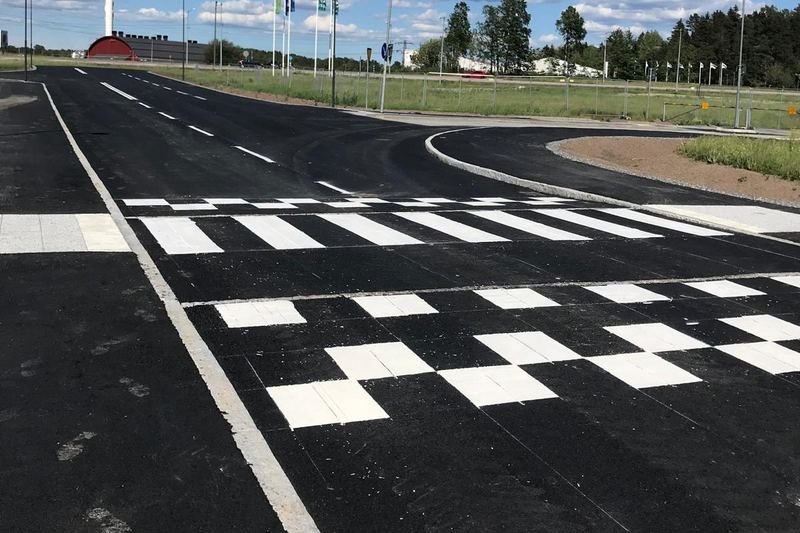 Nymålat övergångsställe och ett farthinder med vita schackrutor på svart asfalt, med en vit kantlinje längs vägen.
