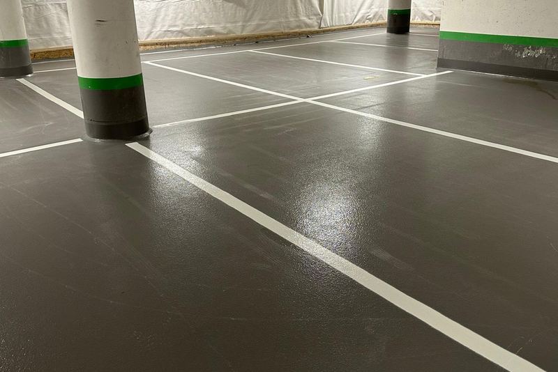 Vita linjer delar in ett grått garagegolv i parkeringsrutor mellan vita pelare med grön rand.