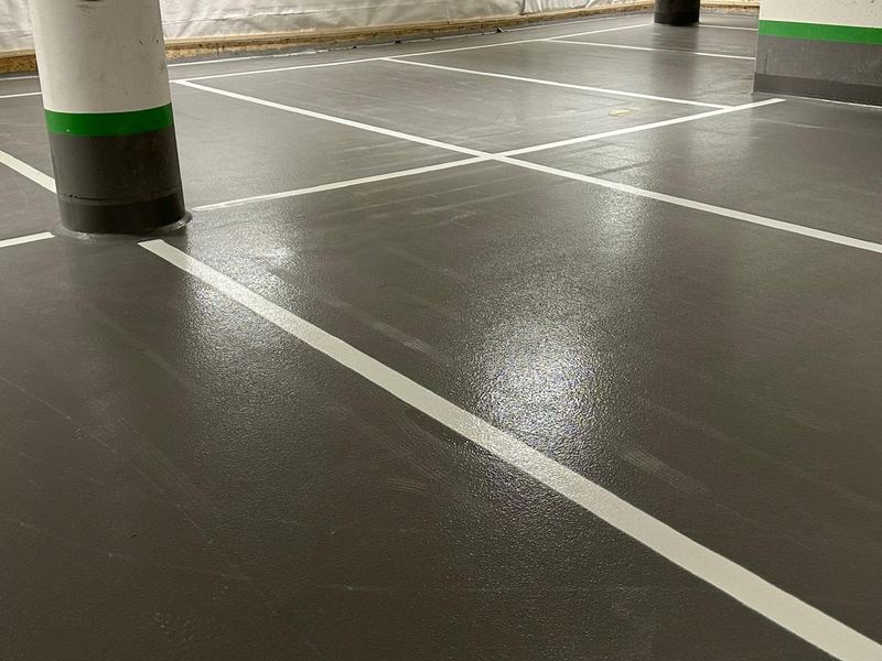 Vita linjer delar in ett grått garagegolv i parkeringsrutor mellan vita pelare med grön rand.