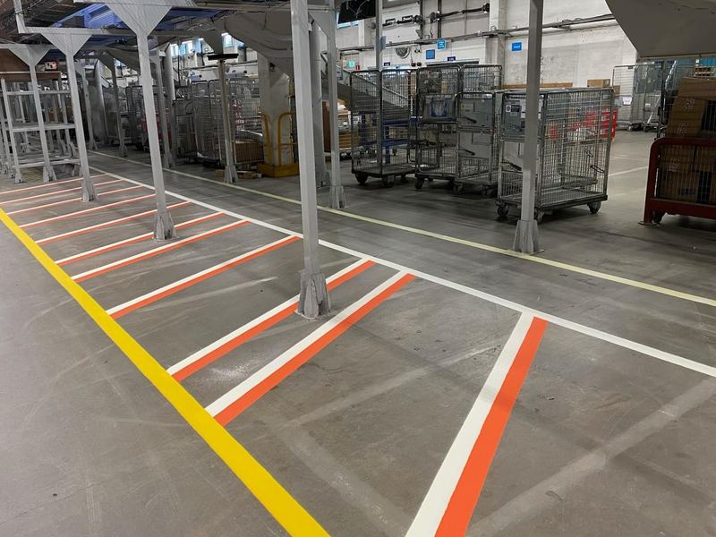 Gula, vita och orange linjer på betonggolvet i en stor inomhushall med rullburar.