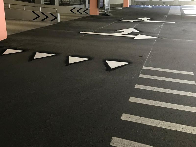Vita svängpilar, en rad väjningstrianglar och breda vita ränder på asfalten i ett parkeringshus.