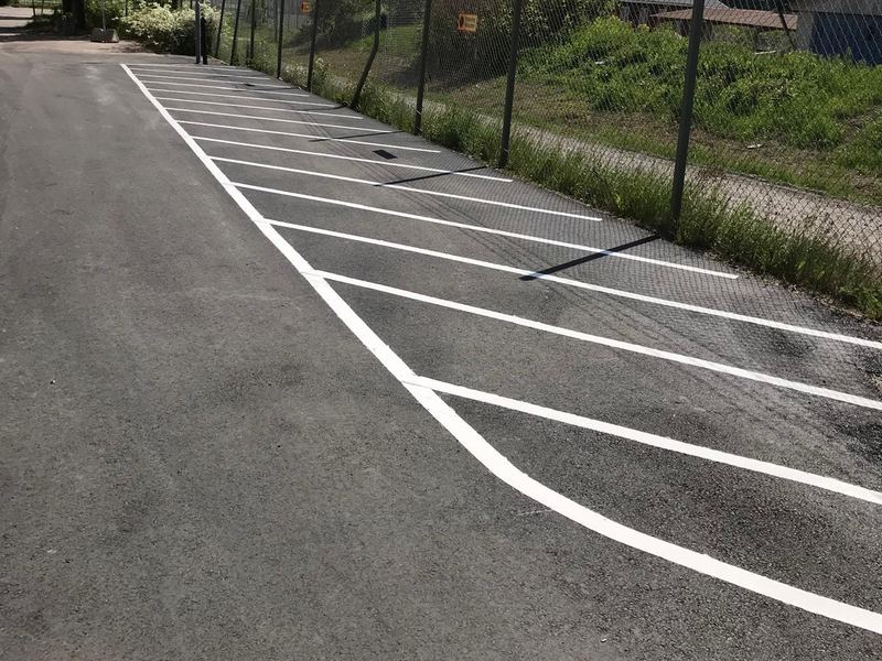 Vita linjer för snedställda parkeringsplatser på asfalt längs ett staket.